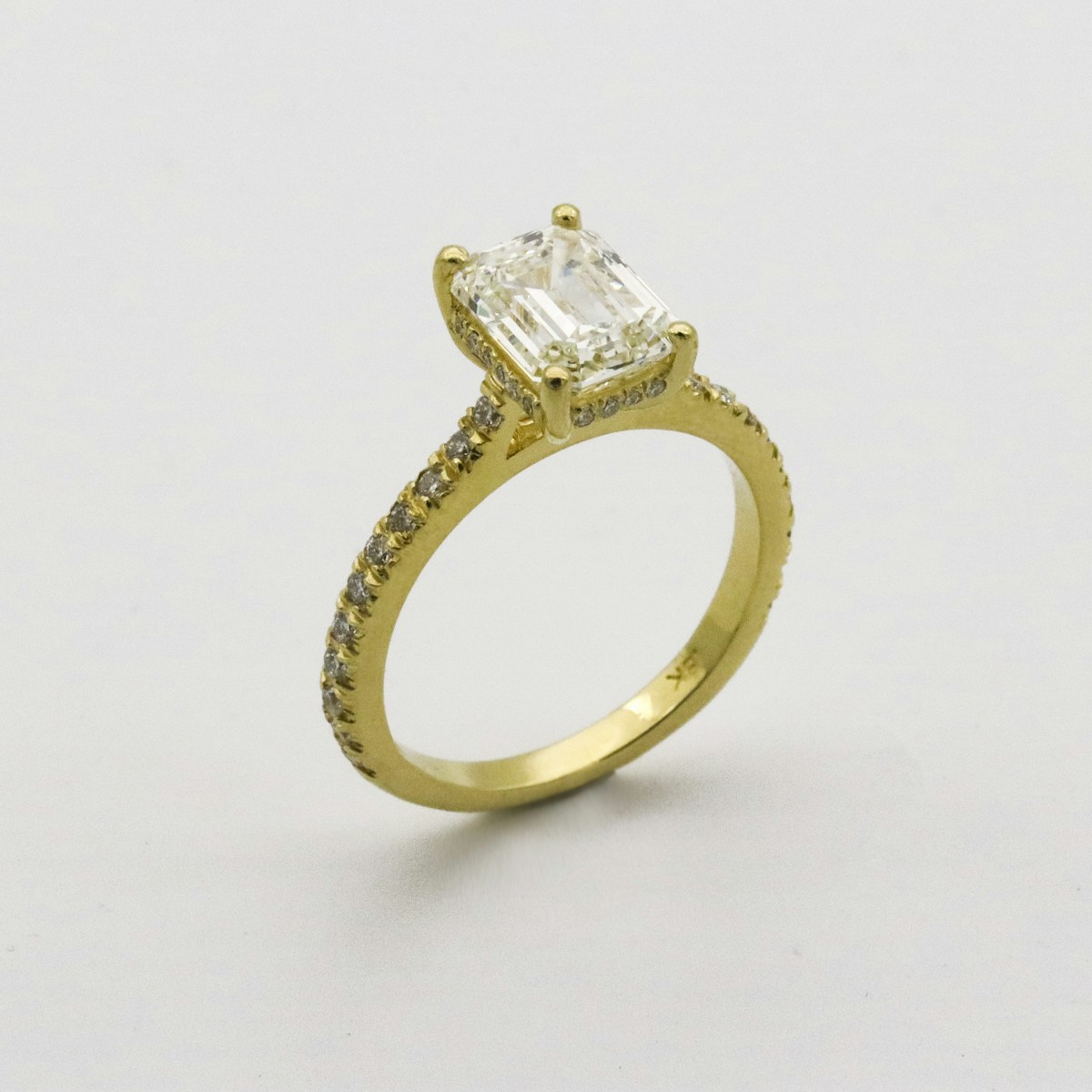A yellow gold ring with an emerald-cut diamond and pavé diamond band