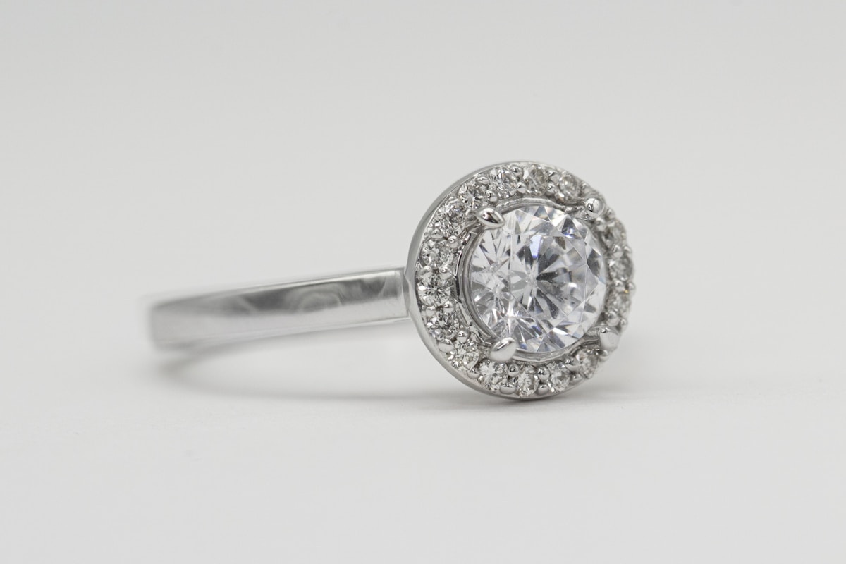 A round diamond halo engagement ring on a white background