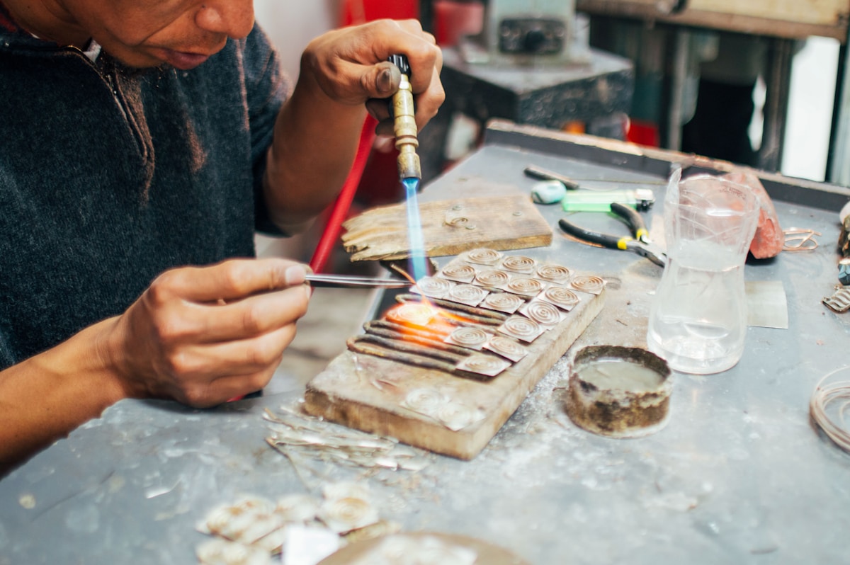An artisan using a torch to hand-craft gold jewelry pieces at a workbench