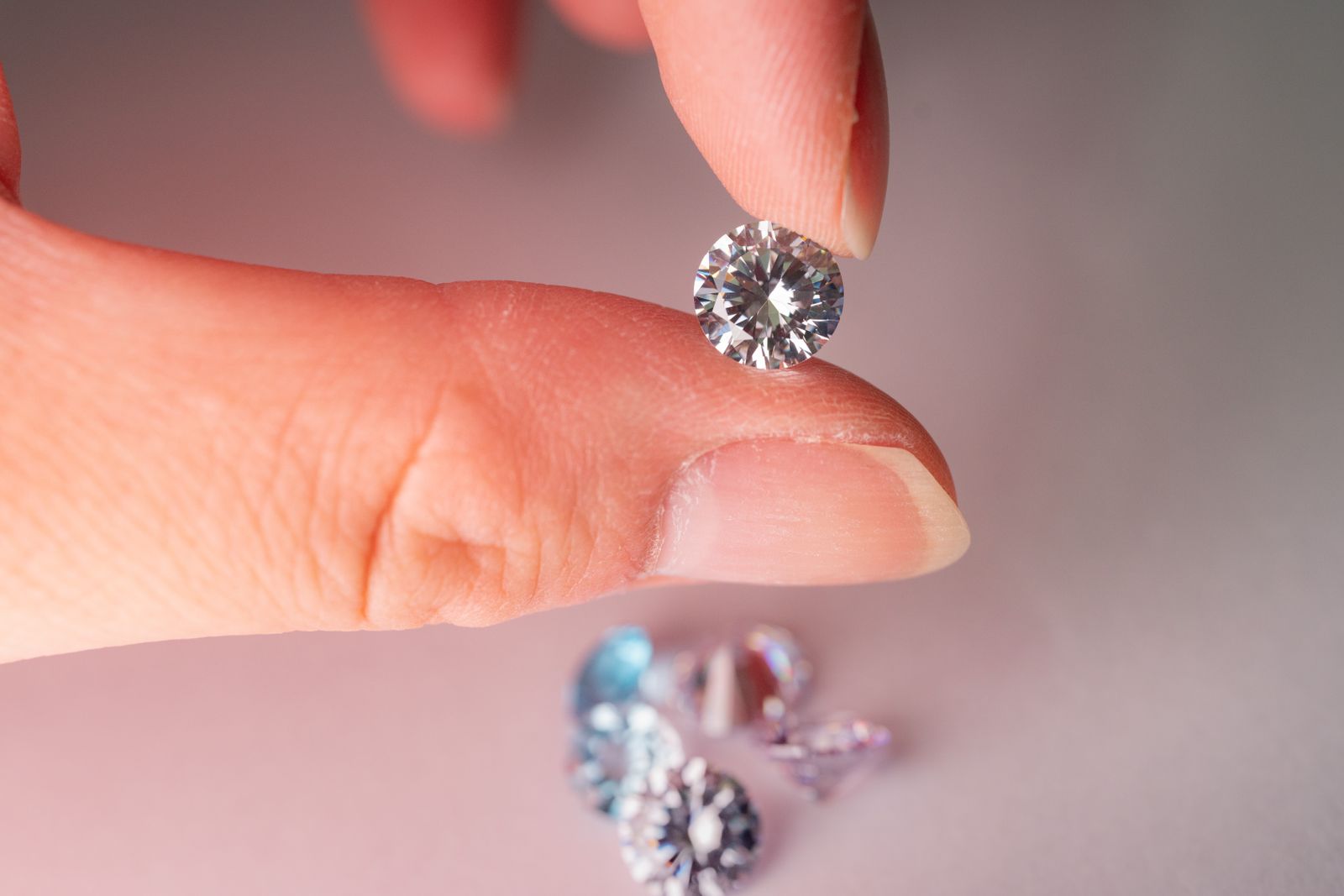 A loose round brilliant-cut diamond held between two fingers, with more loose diamonds below
