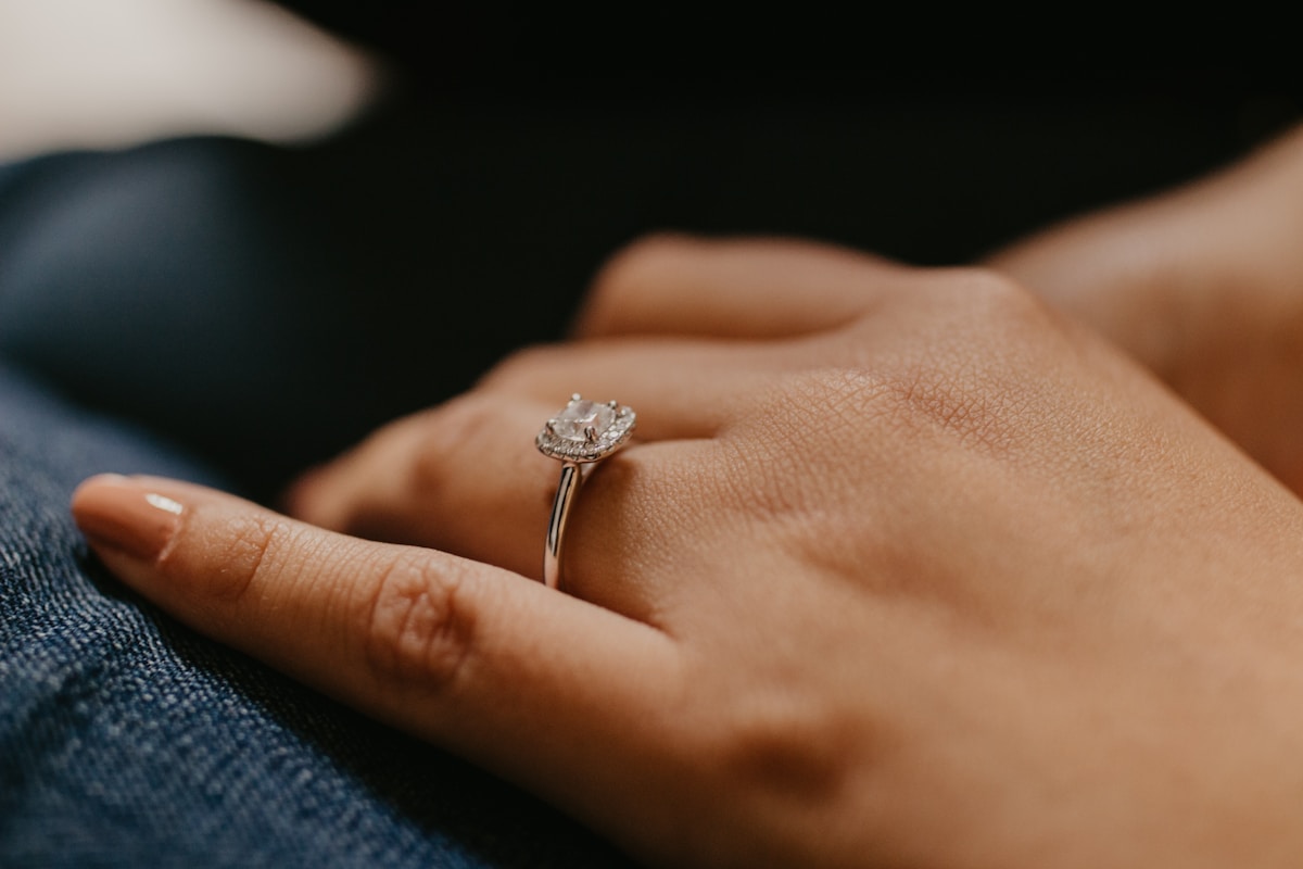 A woman's hand wearing a halo engagement ring, resting casually