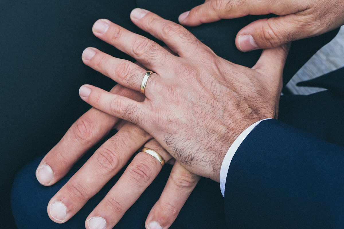 Two men's hands stacked, each wearing a gold wedding band